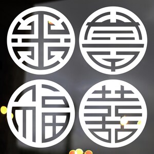 May include: Four white circular designs with intricate patterns. Each design is enclosed within a circle, featuring a unique arrangement of lines and shapes. The designs are set against a dark background, with a hint of a wooden frame.