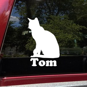May include: White silhouette of a cat sitting on a black background with the name "Tom" written below it.