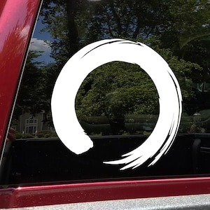 May include: White vinyl decal of a stylized circle with a brushstroke design. The circle is incomplete, creating a sense of movement and flow. This decal is perfect for adding a touch of Zen to any surface.