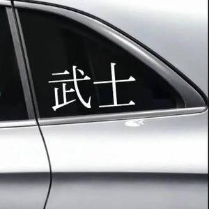 May include: White vinyl decal featuring the Japanese characters for "Samurai". The decal is displayed on a car window, with the characters prominently visible against the dark glass. The sticker is designed for vehicle decoration.