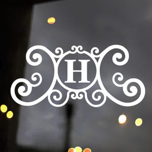 May include: White decorative monogram featuring the letter "H" in a circular frame, surrounded by ornate scrollwork. The design is symmetrical and elegant, suitable for personalization or home decor.