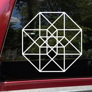 May include: White geometric design decal on a car window. The design features a complex pattern of interconnected squares, octagons, and diagonal lines. The decal is applied to the window of a red vehicle, with a blurred background of trees and a house.