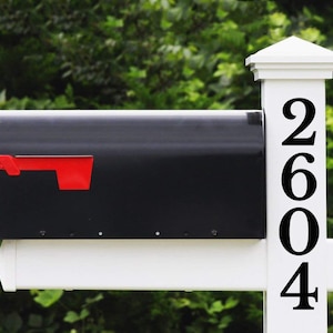 May include: Black mailbox with a red flag attached to a white post with black numbers 2604 on the post.