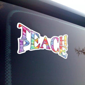 Teach Peace sticker against a black background, highlighting the vivid tie-dye colors and clarity of the text.