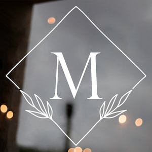 May include: A white monogram with the letter "M" in a diamond shape with two stylized leaves on either side of the letter.