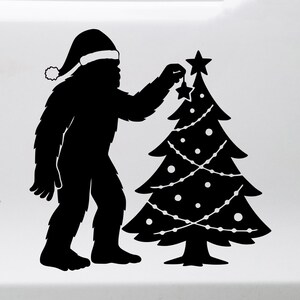 May include: Black silhouette of a Bigfoot wearing a Santa hat, decorating a Christmas tree with star ornaments. The tree is adorned with lights and round ornaments. A festive holiday design.