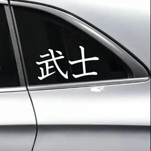 May include: White vinyl decal featuring the Japanese characters for "Samurai". The decal is applied to the window of a vehicle, with the characters prominently displayed against the dark glass.