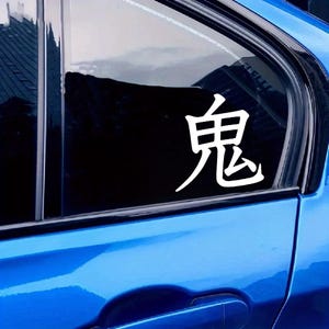 May include: White Japanese Kanji character sticker applied to a blue car window. The character is a bold, stylized symbol, likely for decoration or personalization. The car's paint is a bright, glossy blue.