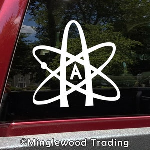 May include: White vinyl decal featuring a stylized atom symbol with the letter "A" in the center. The design is applied to a vehicle window, with a red truck bed visible below. The decal is a symbol of atheism.