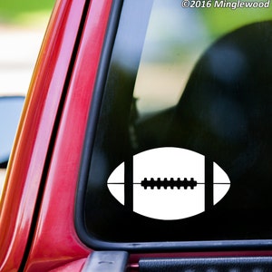 May include: White vinyl decal of a football on a red car window. The decal is a simple outline of a football with laces.