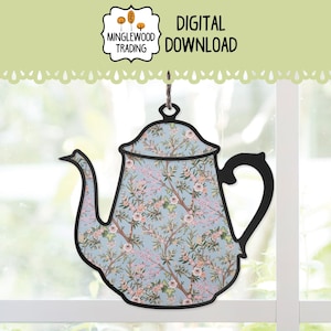 Puede incluir: Un letrero decorativo con forma de tetera con un estampado floral en tonos rosa, blanco y verde sobre un fondo azul claro. El letrero tiene un contorno y un asa negros, con las palabras "DIGITAL DOWNLOAD".