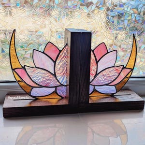 Könnte beinhalten: Ein Buchstützen-Set mit Lotusblumen aus Buntglas. Die Buchstützen haben einen Holzsockel und eine zentrale Stütze. Das Lotusblumen-Design enthält rosa, orange und goldene Farbtöne. Der Text "Bones & Bevels" ist auf dem Sockel zu sehen.