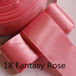 May include: A roll of pink satin ribbon and a length of the same ribbon, with the text "18 Fantasy Rose". The ribbon has a smooth, shiny surface and is a soft, muted pink color. The ribbon is likely used for crafts, gift wrapping, or decorative purposes.
