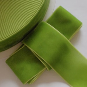 May include: A roll of bright green velvet ribbon with a soft, plush texture. The ribbon is unwound in sections, revealing its smooth, shiny surface. The ribbon is a vibrant, solid color, perfect for crafts and embellishments.
