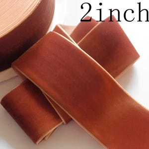 Puede incluir: Primer plano de un rollo de cinta de terciopelo color óxido. La cinta mide 5 cm de ancho. El texto "2inch" está impreso en negro en la imagen. La cinta está doblada sobre sí misma en primer plano.