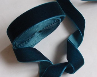 May include: A roll of teal velvet ribbon with a soft, plush texture. The ribbon is unwound, revealing a smooth, satin-like backing. The ribbon's color is a deep, rich teal, perfect for crafting and decorative projects.