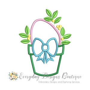 May include: A green, blue, and pink floral basket design. The basket has a blue bow, a pink handle, and is decorated with green leaves and yellow berries. The text "Everyday Designs Boutique" is at the bottom.