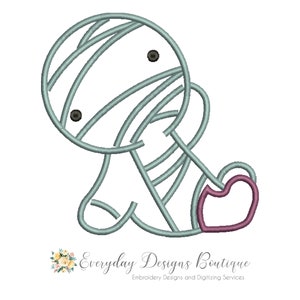 May include: A light blue and white striped mummy with black eyes and a pink heart. The mummy is sitting with its legs crossed and its arms folded.