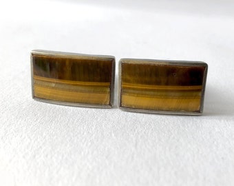 May include: A pair of silver cufflinks with tiger's eye stone insets. The stones have a brown, gold, and black striped pattern.