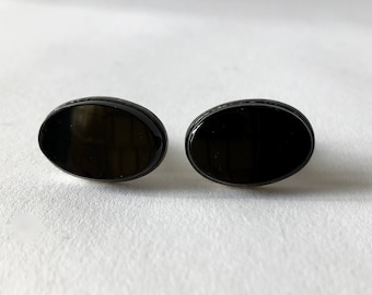 May include: A pair of black oval cufflinks. The cufflinks are made of a smooth, shiny material.