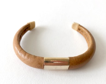 May include: A tan leather bracelet with a gold metal bar accent.