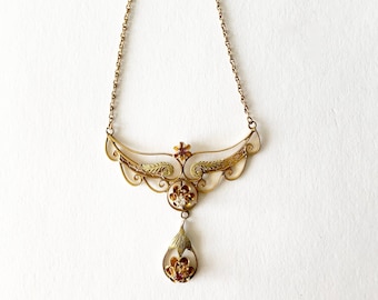 May include: A gold necklace with a delicate, ornate pendant featuring a floral design with small red and white stones. The pendant hangs from a delicate chain.