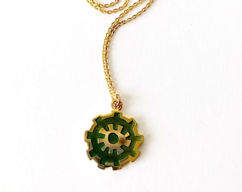 May include: A gold chain necklace with a green and gold pendant. The pendant is a circular design with a sun-like symbol in the center.