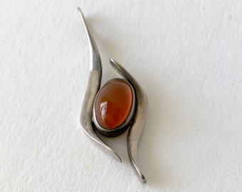 May include: A silver pendant with an orange gemstone set in a modern abstract design.