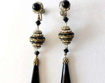 May include: A pair of black and gold dangle earrings with a black teardrop-shaped crystal at the bottom. The earrings have a clip-on closure.