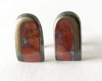 May include: A pair of silver cufflinks with red and white agate stone insets. The cufflinks are in the shape of an arch.