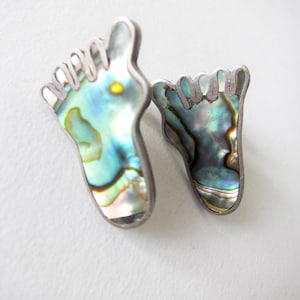 May include: A pair of silver earrings shaped like feet, with iridescent abalone shell inlays.