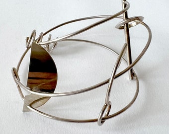 May include: A silver metal bracelet with a geometric design. The bracelet is made of multiple intertwined wires and features a half-circle shape.