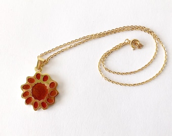 May include: A gold chain necklace with a pendant featuring a circular design with a red center and gold accents.
