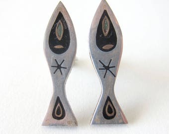 May include: A pair of silver earrings shaped like fish with black and green enamel accents. Each fish has a star design and a teardrop shape at the bottom.