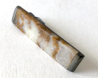 May include: A brown and white agate tie clip with a silver metal clasp.
