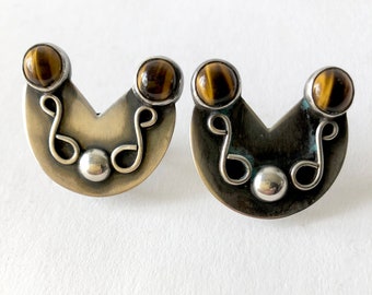 May include: A pair of silver earrings with a crescent moon shape and tiger's eye stones.