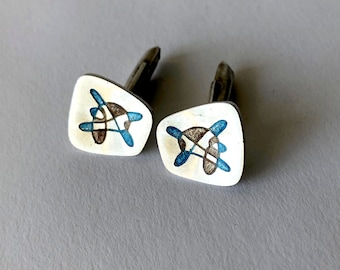 May include: A pair of silver cufflinks with a geometric design in blue, brown, and white.