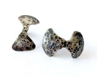 May include: A pair of silver earrings with a textured, hammered finish. The earrings are shaped like a bow tie.