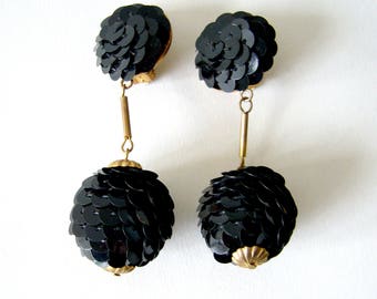 May include: A pair of dangle earrings with black sequin ball and flower-shaped tops. The earrings have gold-tone metal accents.