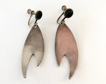 May include: A pair of silver tone clip-on earrings with a teardrop shape and a cut-out design.