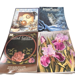 May include: Four books with colorful covers. Titles include "Country Classics," "Bitterroot Backroads 2," "Second Nature 2," and "Realistic Techniques." The books feature images of a wolf, flowers, and rustic scenes. The bottom book has the text "Tavern Boards, Signs & More."