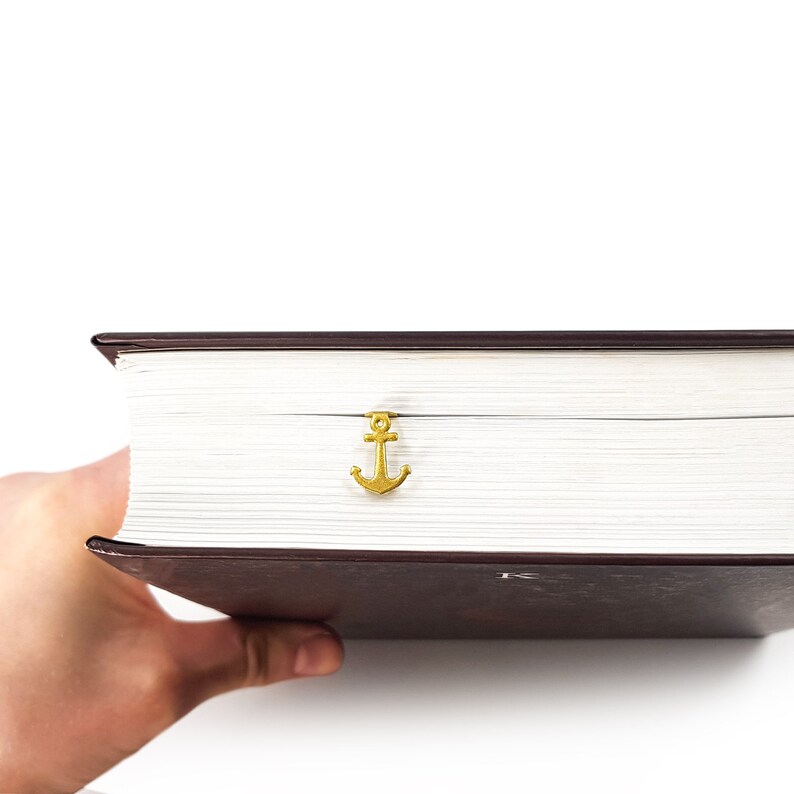 May include: A thick, brown book with a gold anchor bookmark. The book is being held by a hand.