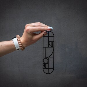 Close-up of a hand holding a black metal Bauhaus-style bookmark against a dark background — sleek geometric design for modern readers.