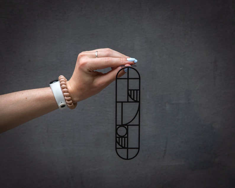 Close-up of a hand holding a black metal Bauhaus-style bookmark against a dark background — sleek geometric design for modern readers.