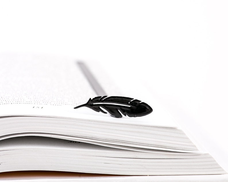 May include: A black feather bookmark on top of a white book with pages turned down.