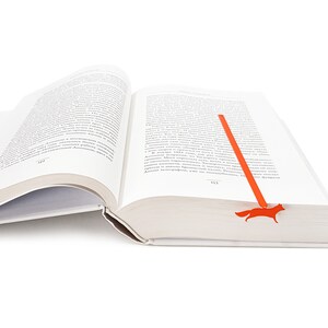 May include: An open book with a red fox bookmark. The bookmark is shaped like a fox and is made of metal.