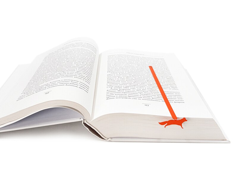 May include: An open book with a red fox bookmark. The bookmark is shaped like a fox and is made of metal.