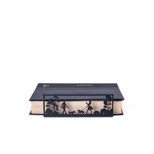 May include: Black metal bookmark with a silhouette design of two people walking dogs in a park. The bookmark is placed on a closed book.