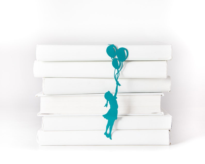 Blue metal bookmark Girl with Balloons. The large silhouette of the girl and the balloons are between the pages of the book. The small balloon is on the side of the book. It is seen even when the book is closed.