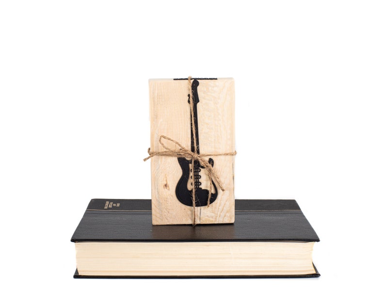 Black metal electric guitar bookmark tied to a wooden block printed with its silhouette and the phrase Reading is good for you, displayed on a closed book. A cool gift for music-loving readers.